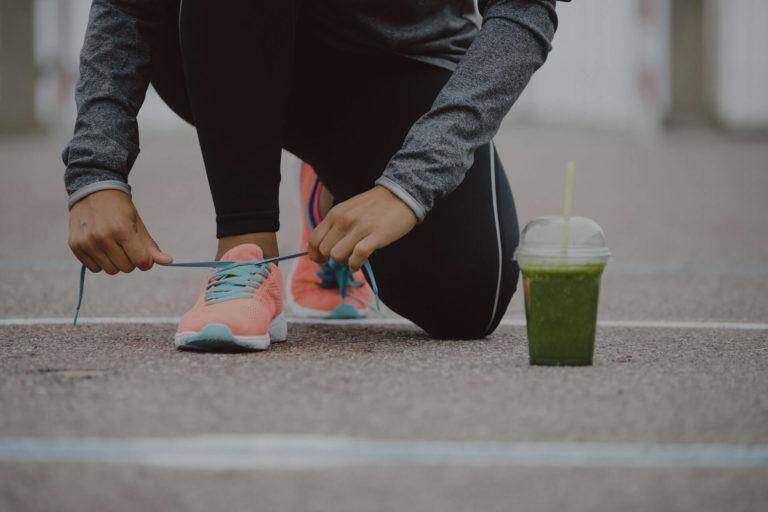 Homme qui fait du sport et qui fait ses lacets avec sa boisson détox posé au sol