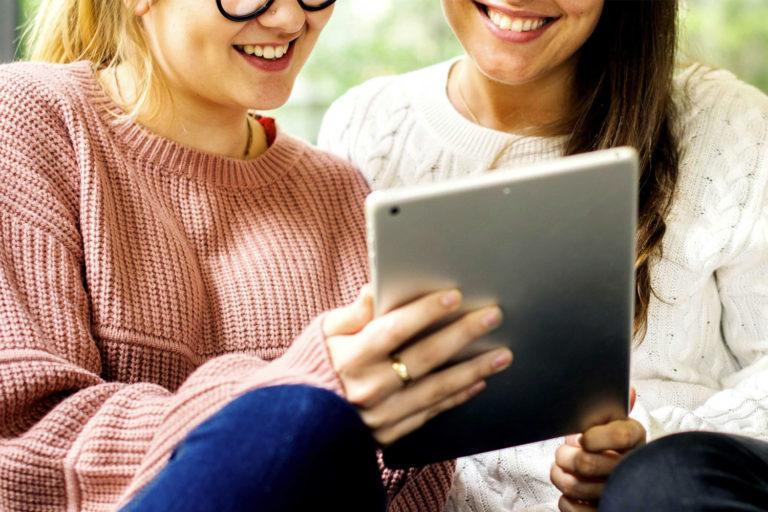 Deux jeunes femmes qui sourient en regardant un iPad