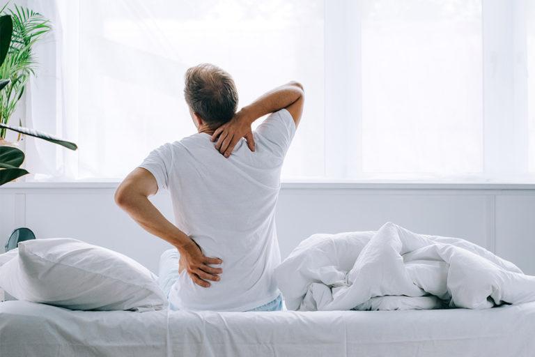 homme vue de dos qui s'étire assis dans sont lit