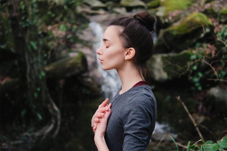 Femme brune qui a les yeux fermés et qui à ses mains posées sur son thorax